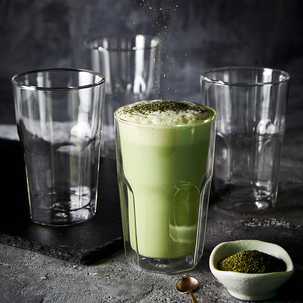 Tall double wall glass filled with green matcha latte and empty glasses in the background - Baccarat
