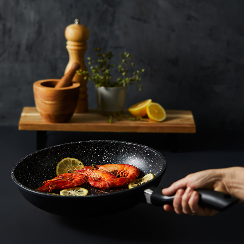 Hand holding a frying pan with grilled salmon and lemon slices - stone frypan 28cm - Baccarat