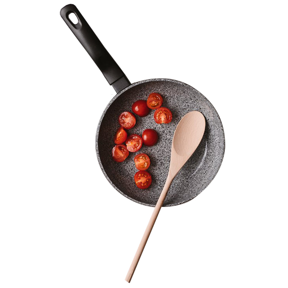 A gray speckled non-stick frying pan with a black handle, shown on a white background with halved cherry tomatoes cooking inside and a light wood spoon resting across the pan.