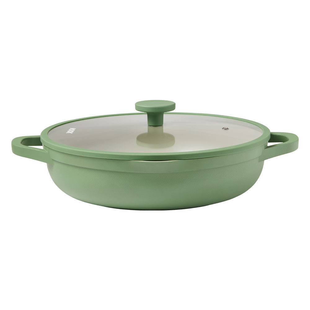 A shallow sage green casserole dish with a clear glass lid is centered against a plain white background.