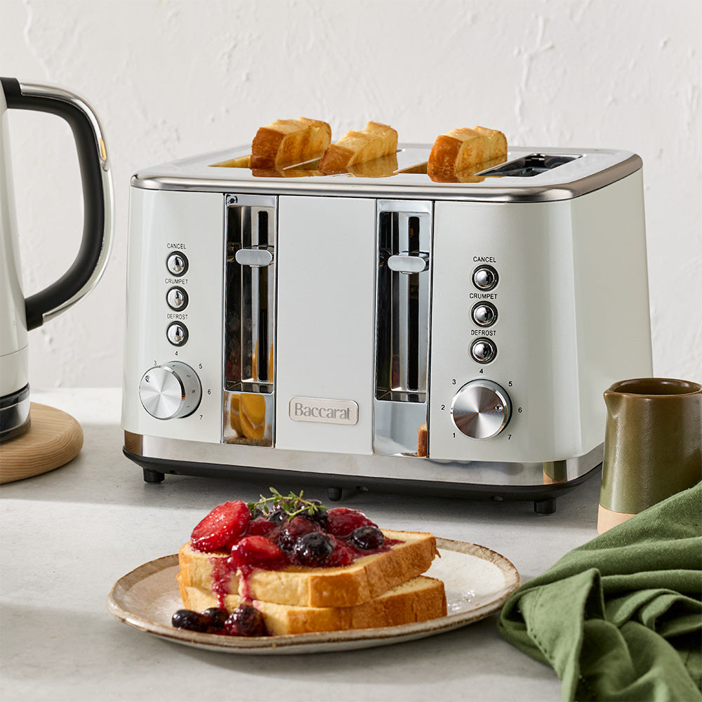A white four-slice toaster filled with toasted bread is placed on a kitchen counter next to a plate of waffles.