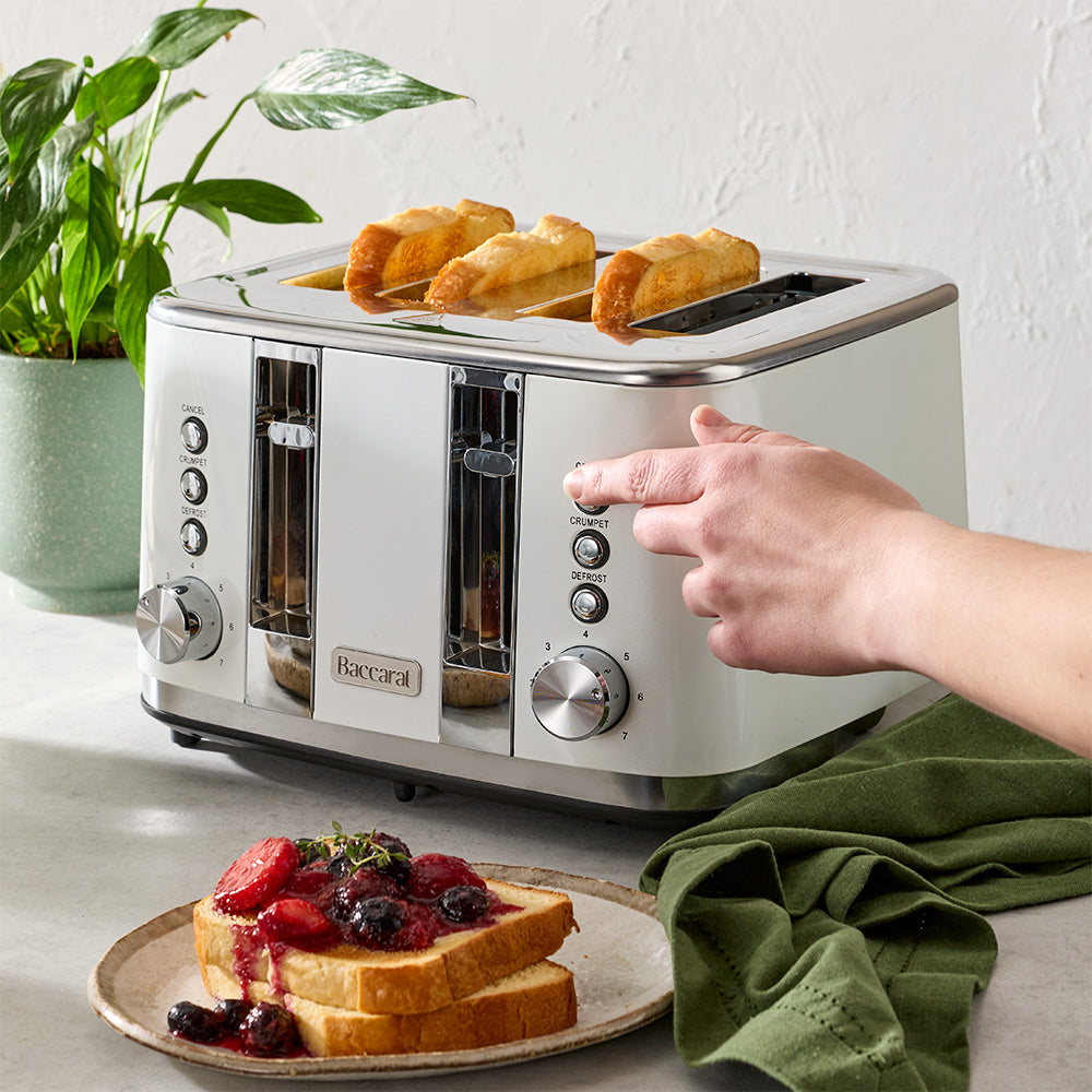 A person's hand is pressing down a lever on a white four-slice toaster filled with toast on a kitchen counter.