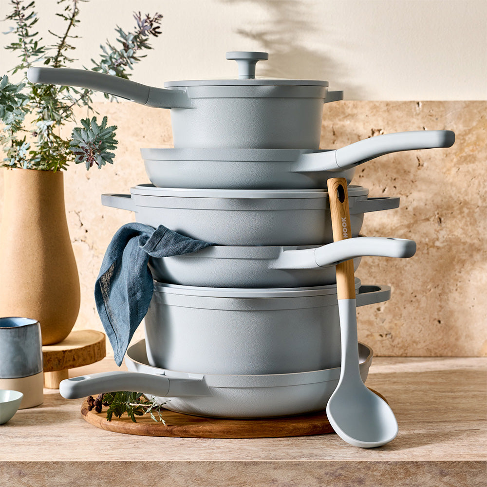 A neat stack of light blue cookware pieces is arranged on a wooden countertop next to a light blue ladle.