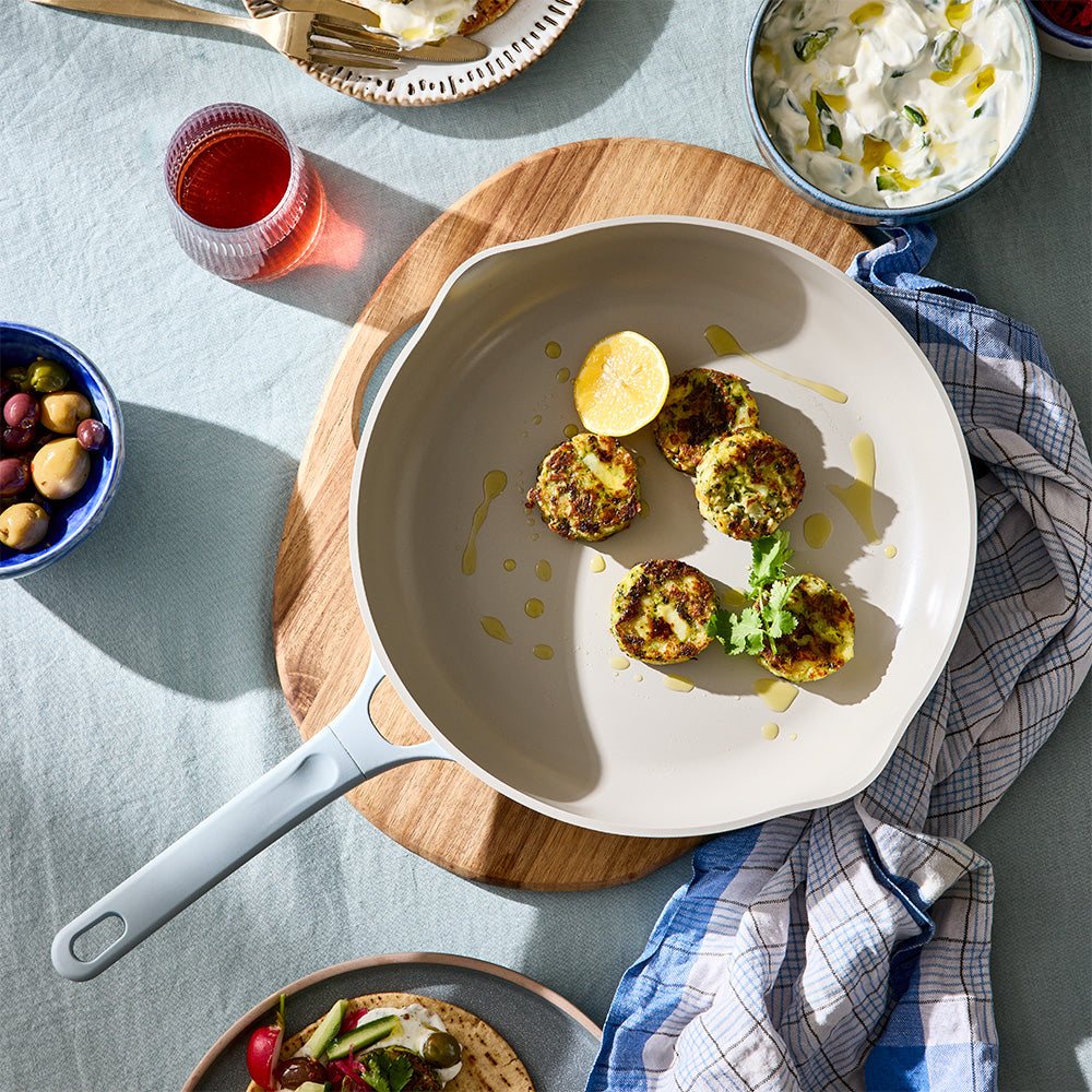 An overhead shot shows a light blue skillet filled with cooked patties set on a wooden trivet on a dining table.
