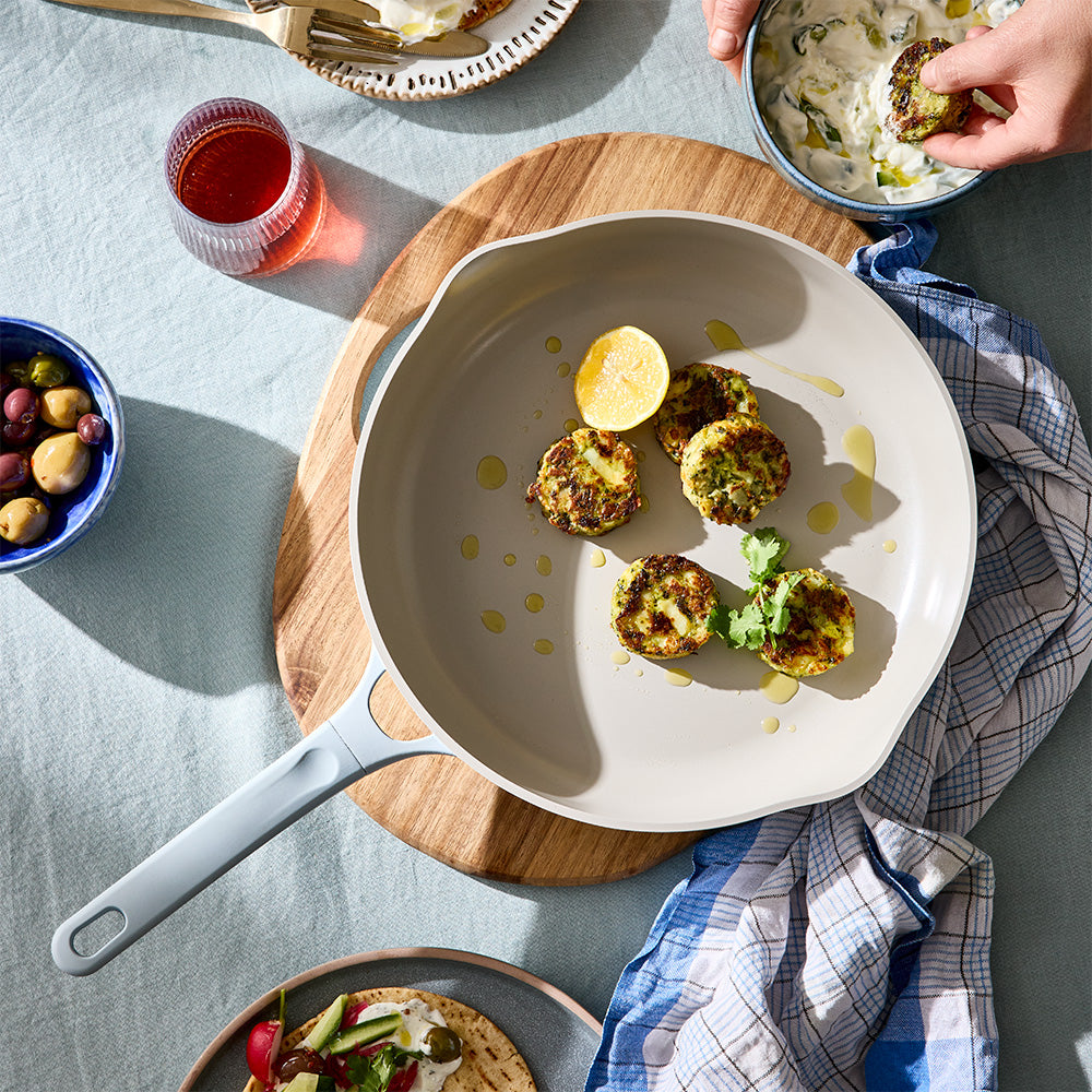 An overhead shot shows a light blue skillet filled with cooked patties on a wooden trivet alongside a blue and white dishcloth.