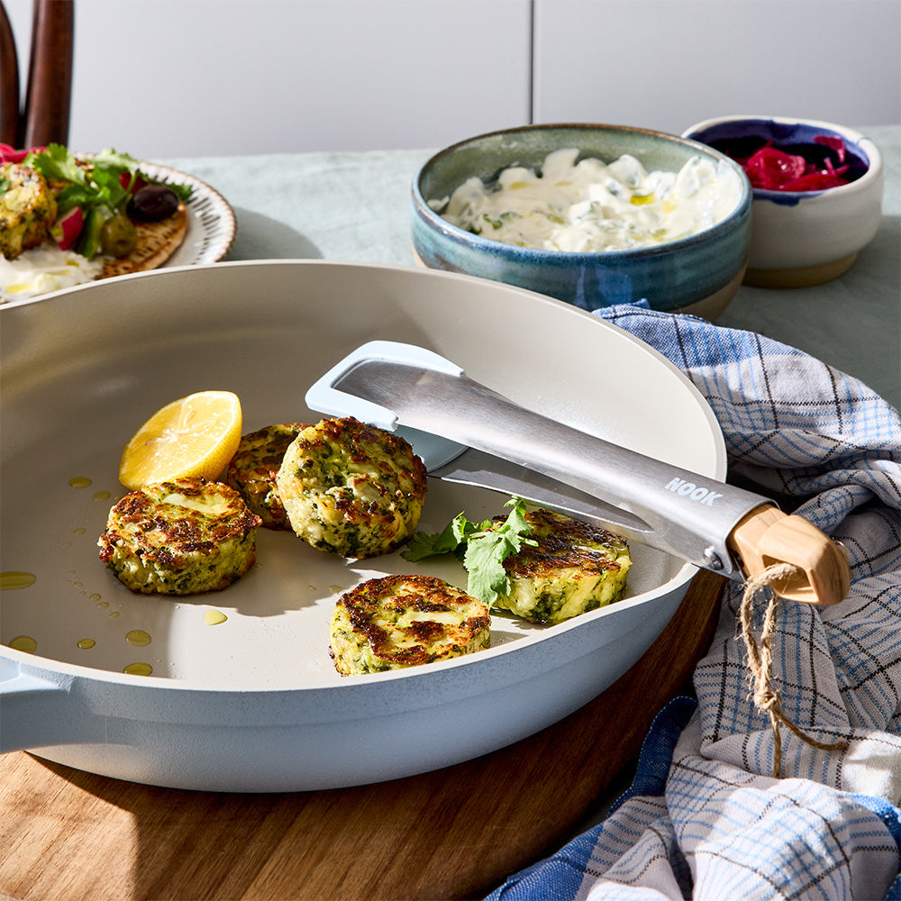 A pair of tongs is resting inside a light blue skillet containing cooked food on a table setup.