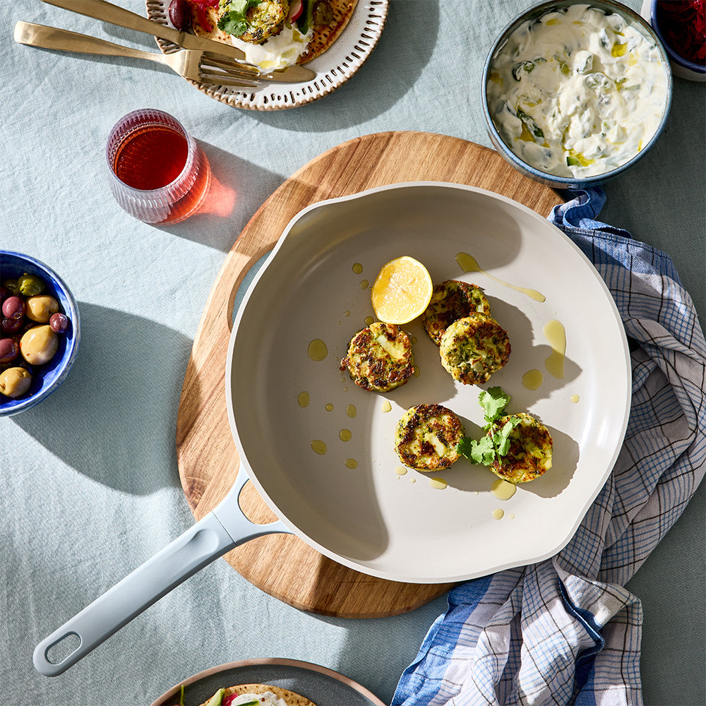 An angled top-down shot shows cooked patties inside a light blue skillet set on a wooden board next to small serving bowls.