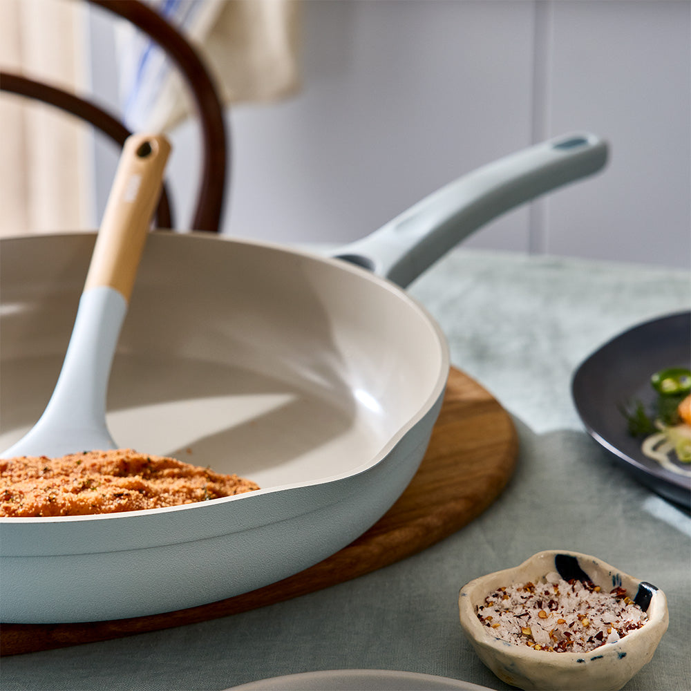A close-up view shows food being stirred inside a light blue frying pan resting on a trivet.