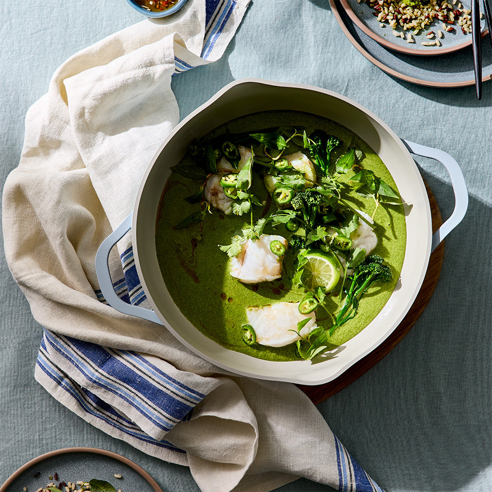 An overhead view shows a light blue cooking pan filled with green curry set on a kitchen towel.