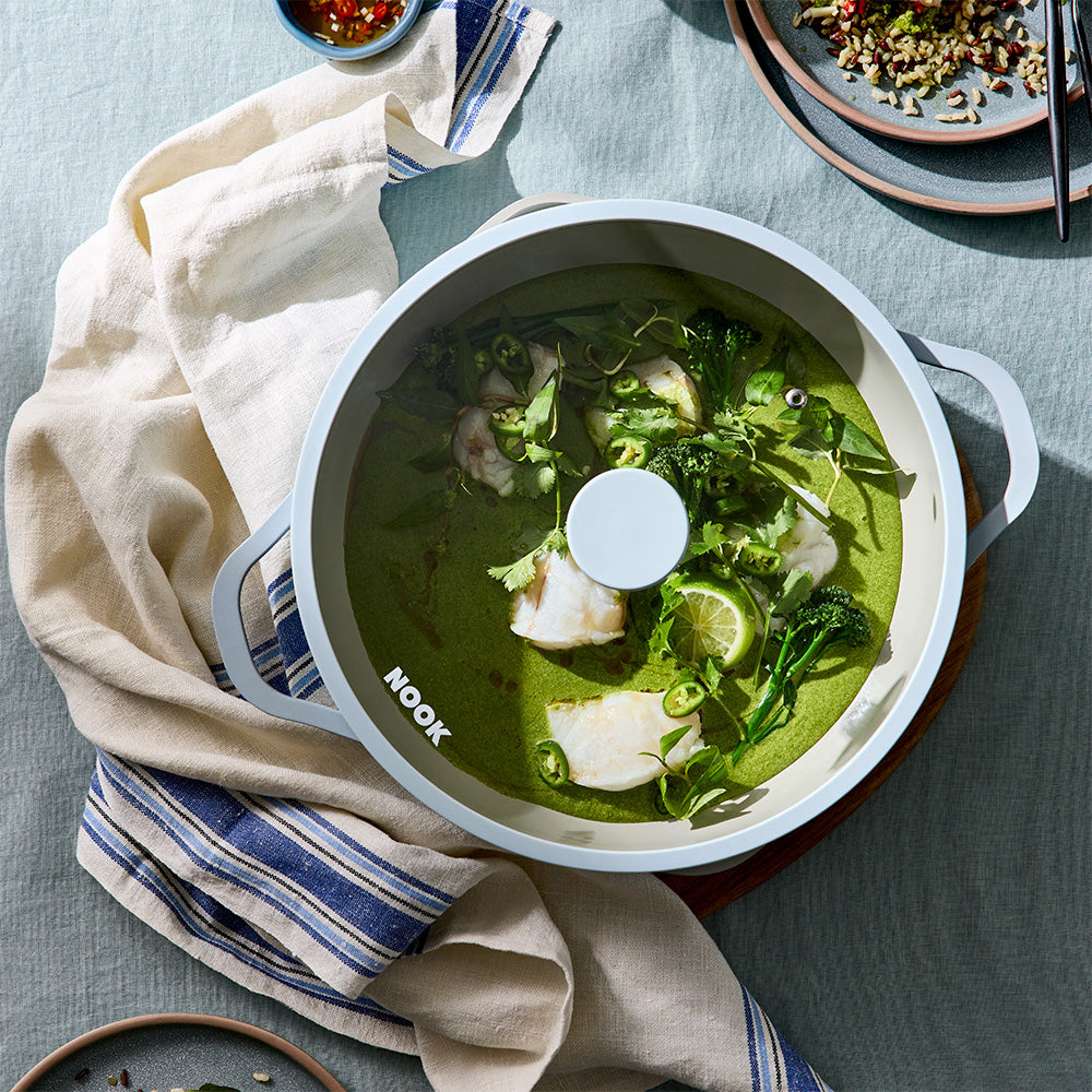A top-down shot shows a light blue pan with cooked green curry resting on a patterned dishcloth.