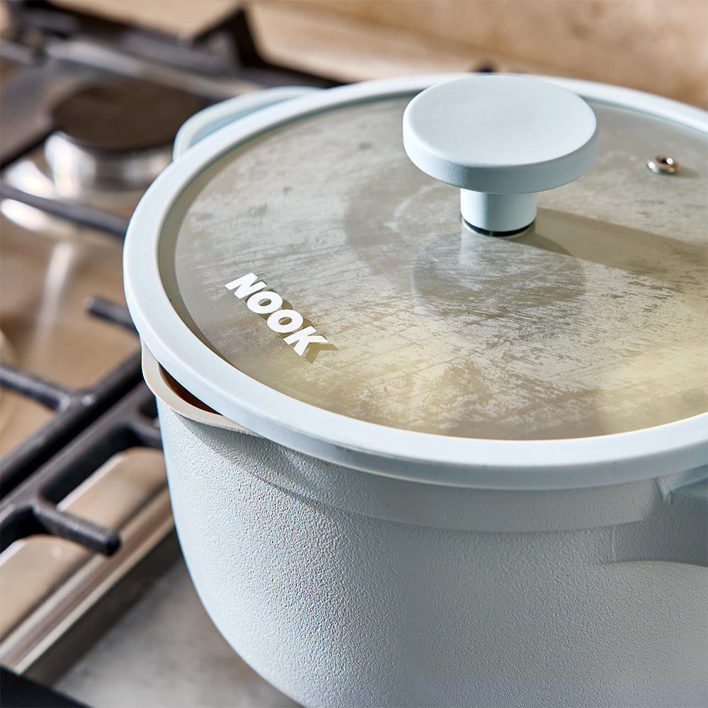 A close-up shot focuses on the glass lid and rim of a light blue saucepan on a stovetop.