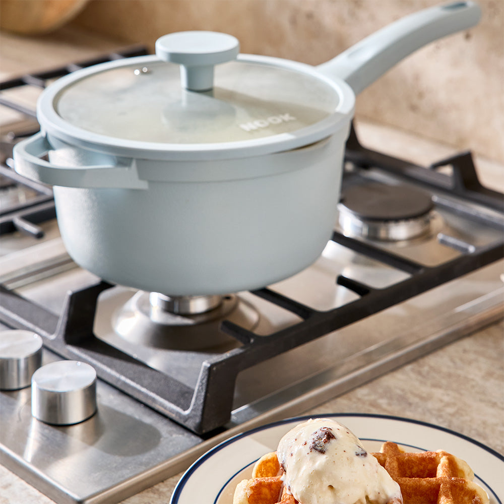 A light blue saucepan is positioned on a stovetop burner next to a plate of waffles.