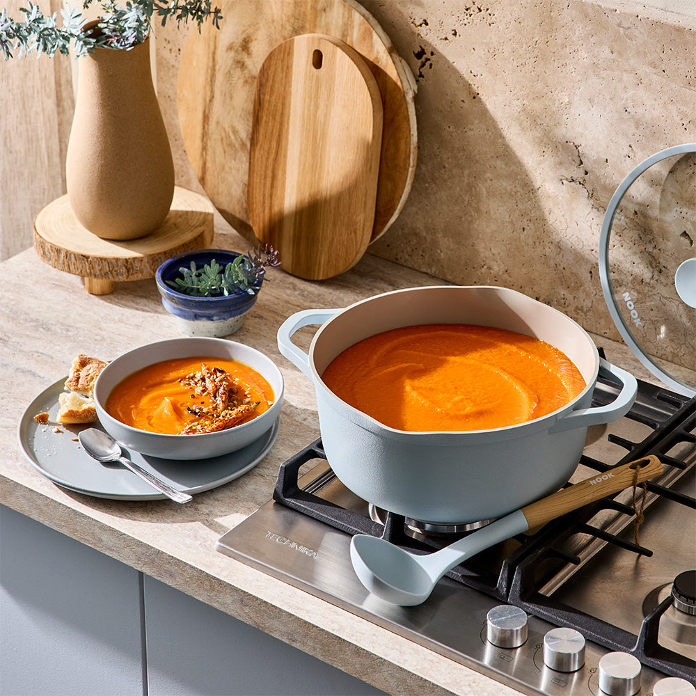 A light blue pot filled with orange soup sits on a stovetop next to a serving bowl.