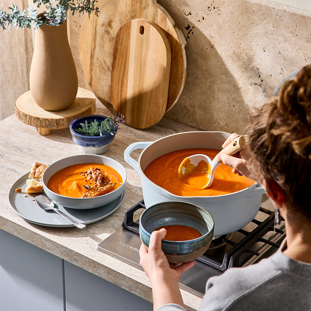 A person is using a ladle to serve soup from a light blue pot into a small bowl.
