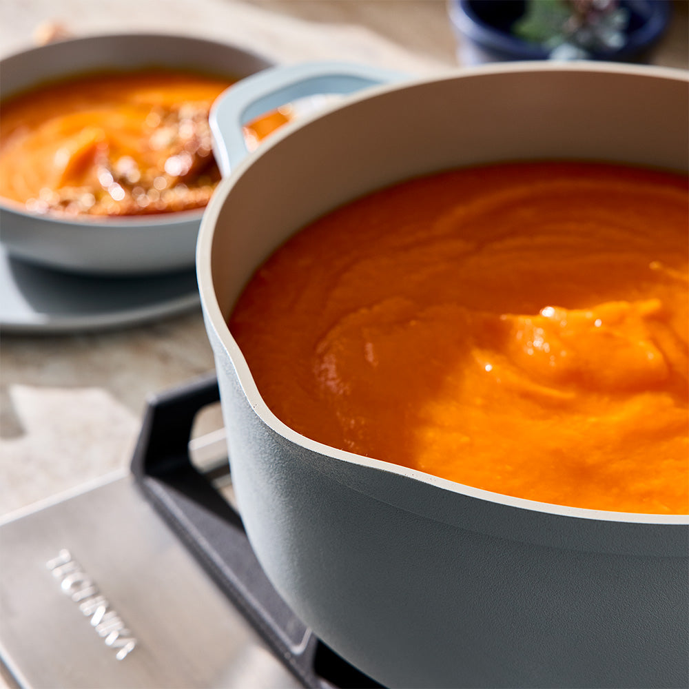 A light blue pot containing orange soup is placed on a stovetop burner.