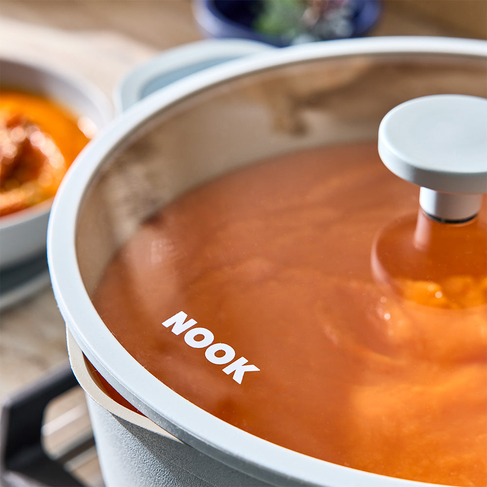 A close-up shot shows the glass lid resting on a light blue pot filled with orange soup.