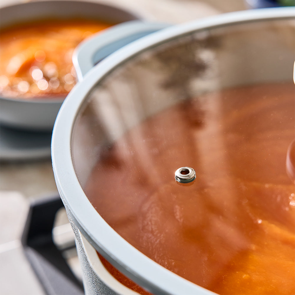 A close-up view focuses on a light blue pot filled with orange soup resting on a cooktop.