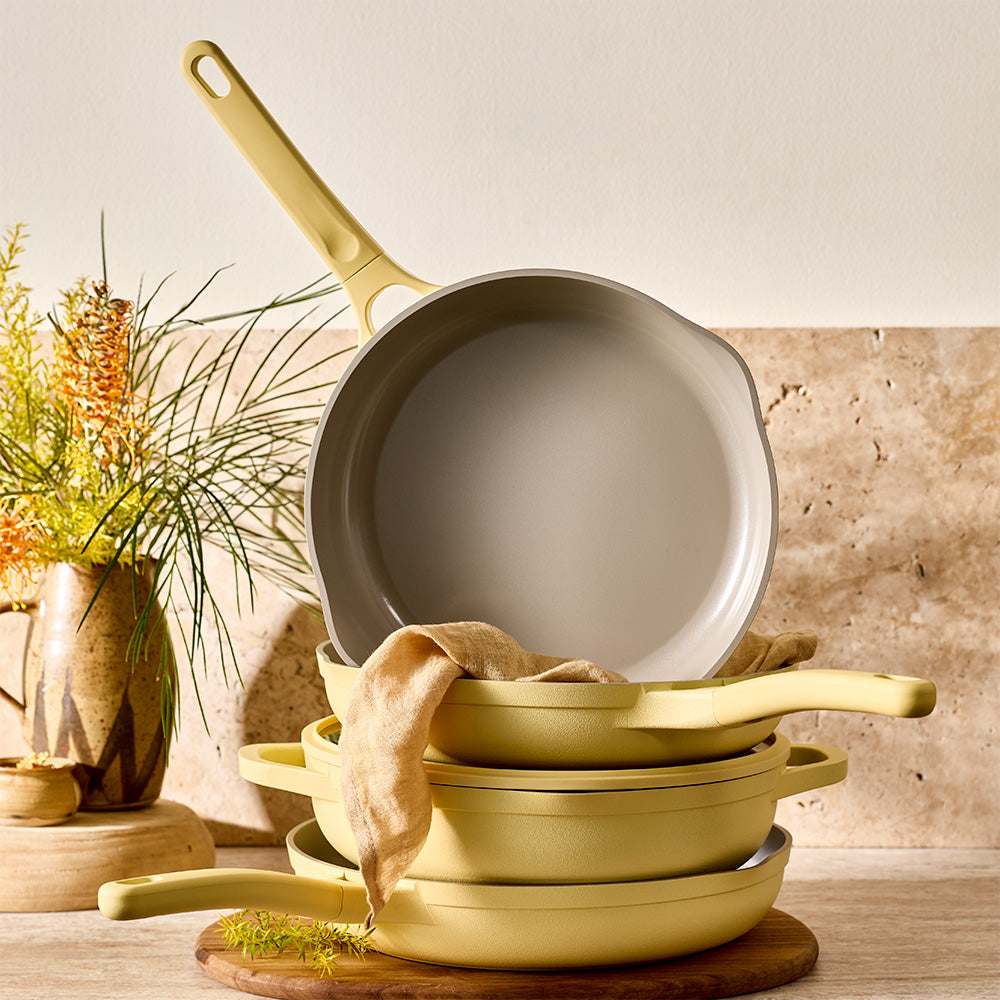 A stack of pastel yellow pots and pans is displayed on a wooden surface against a neutral backdrop.