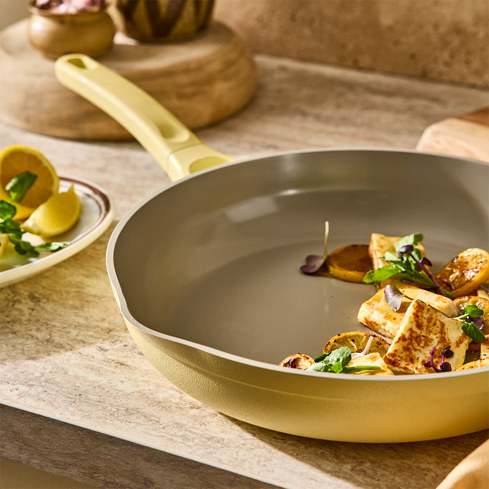 An angled shot shows cooked food served inside a pastel yellow skillet on a wooden countertop.