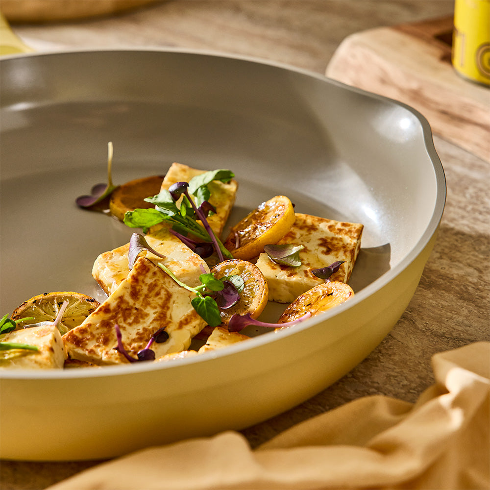 A close-up view shows cooked food garnish inside a pastel yellow skillet with a cream-colored interior.