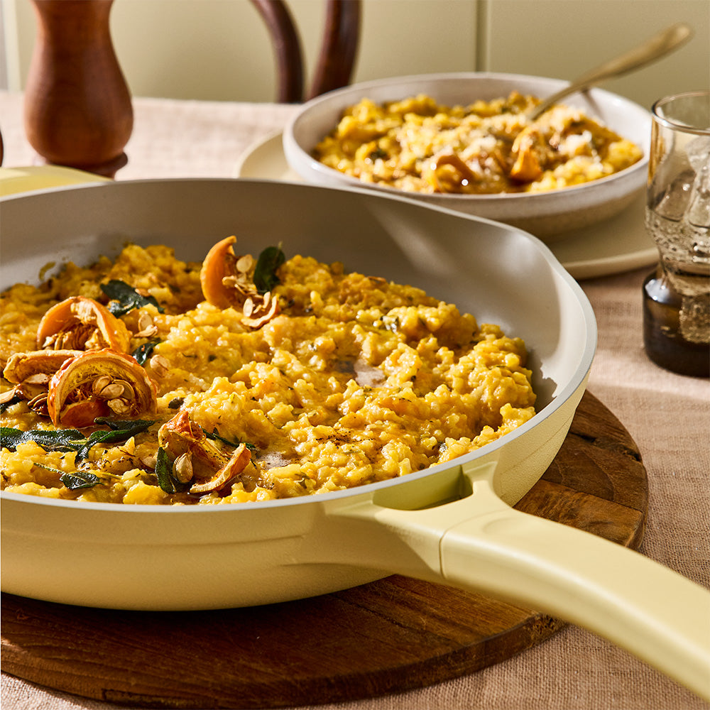 Cooked food inside a pastel yellow skillet is displayed on a dining table with a neutral tablecloth