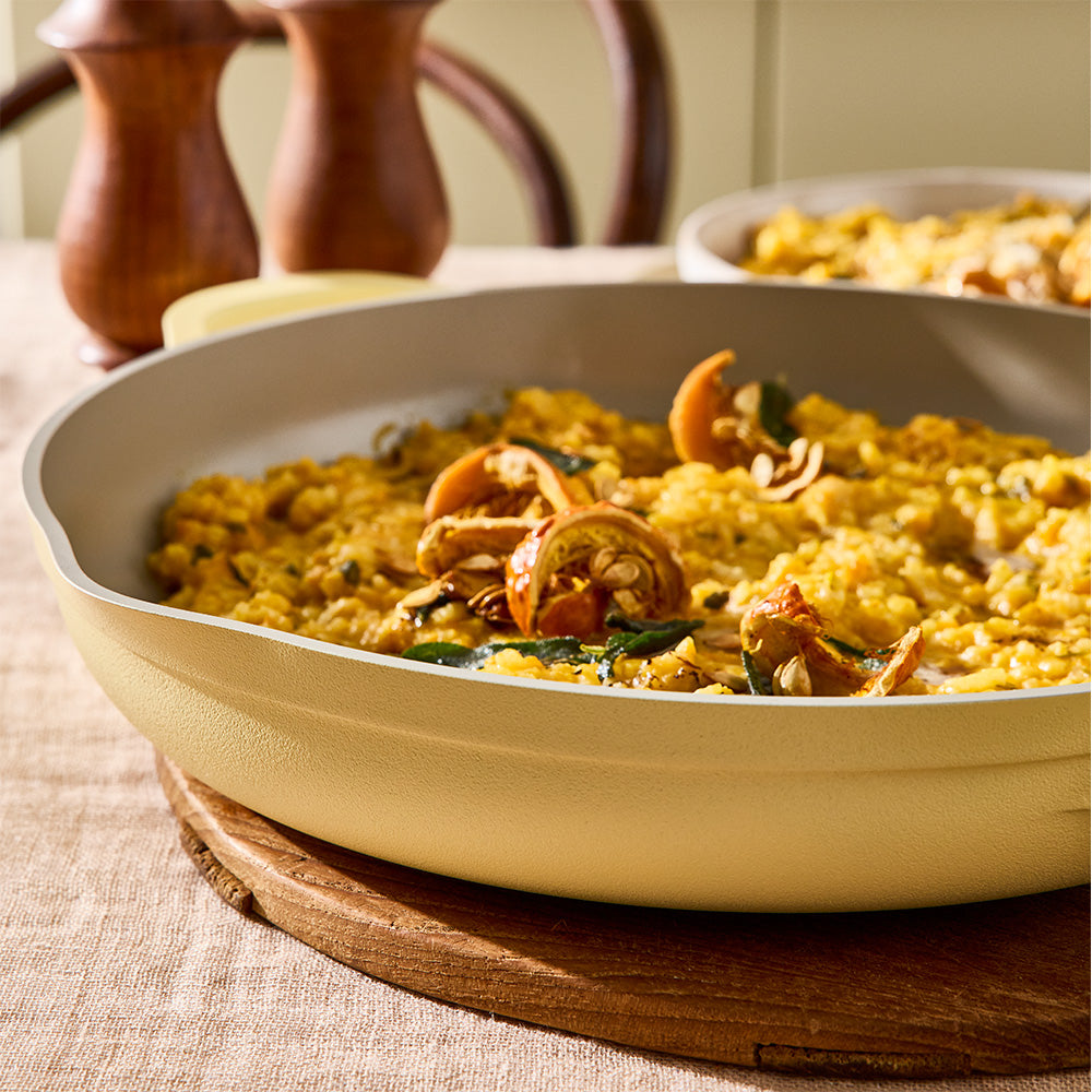 A close-up view shows cooked food inside a pastel yellow skillet set on a wooden board.