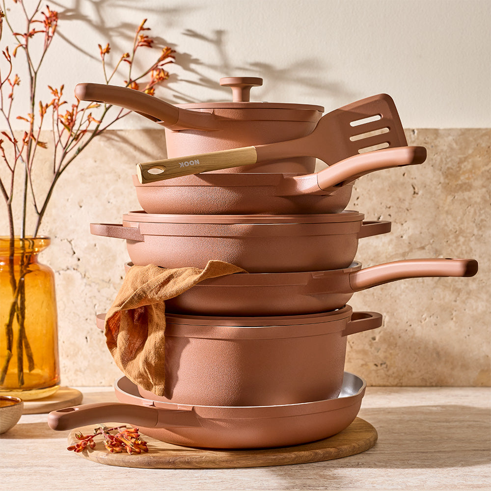 A brown silicone spatula is resting on top of a stack of terracotta-colored pots and pans on a kitchen counter.