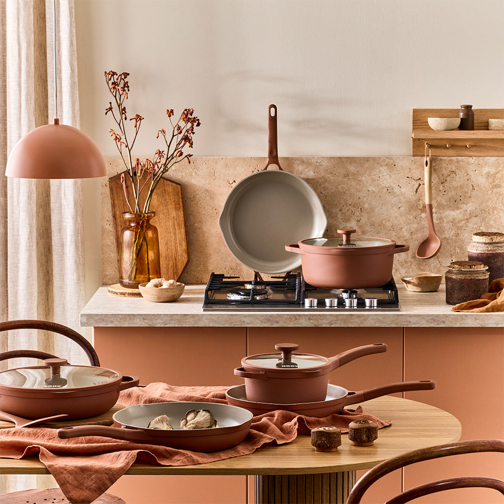 A kitchen table and countertop setup is arranged with terracotta-colored pots, pans, and matching utensils.