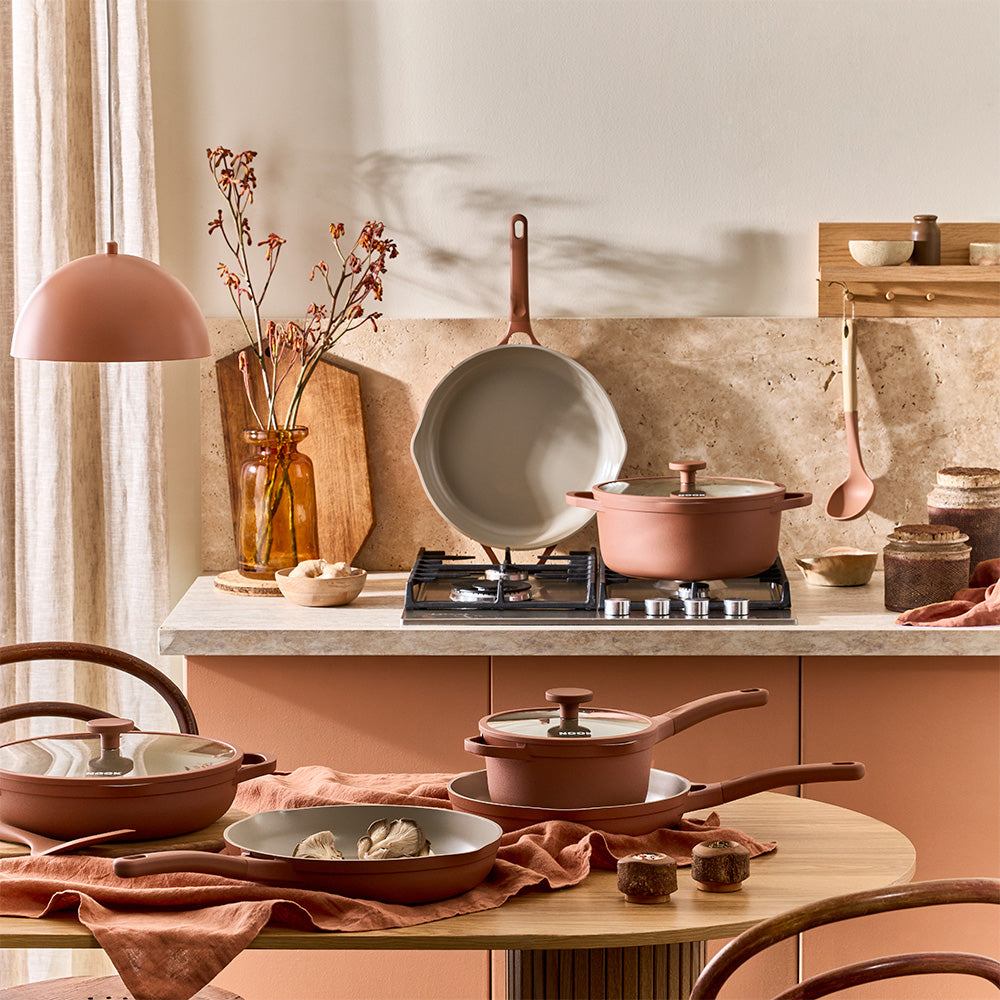 A wide shot shows a decorated kitchen featuring terracotta-colored cookware sets and wooden silicone utensils.