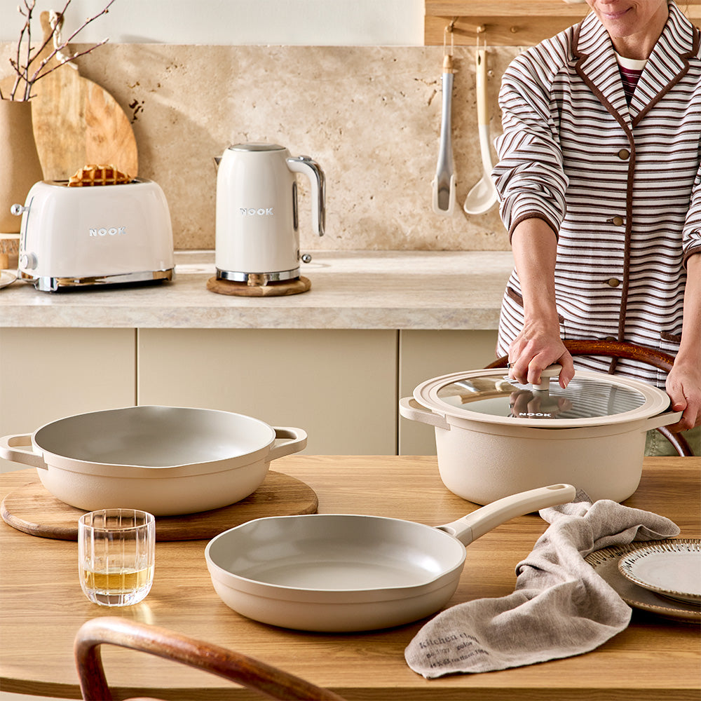 A person in a striped shirt is holding the lid handle of a pot in a bright kitchen environment.