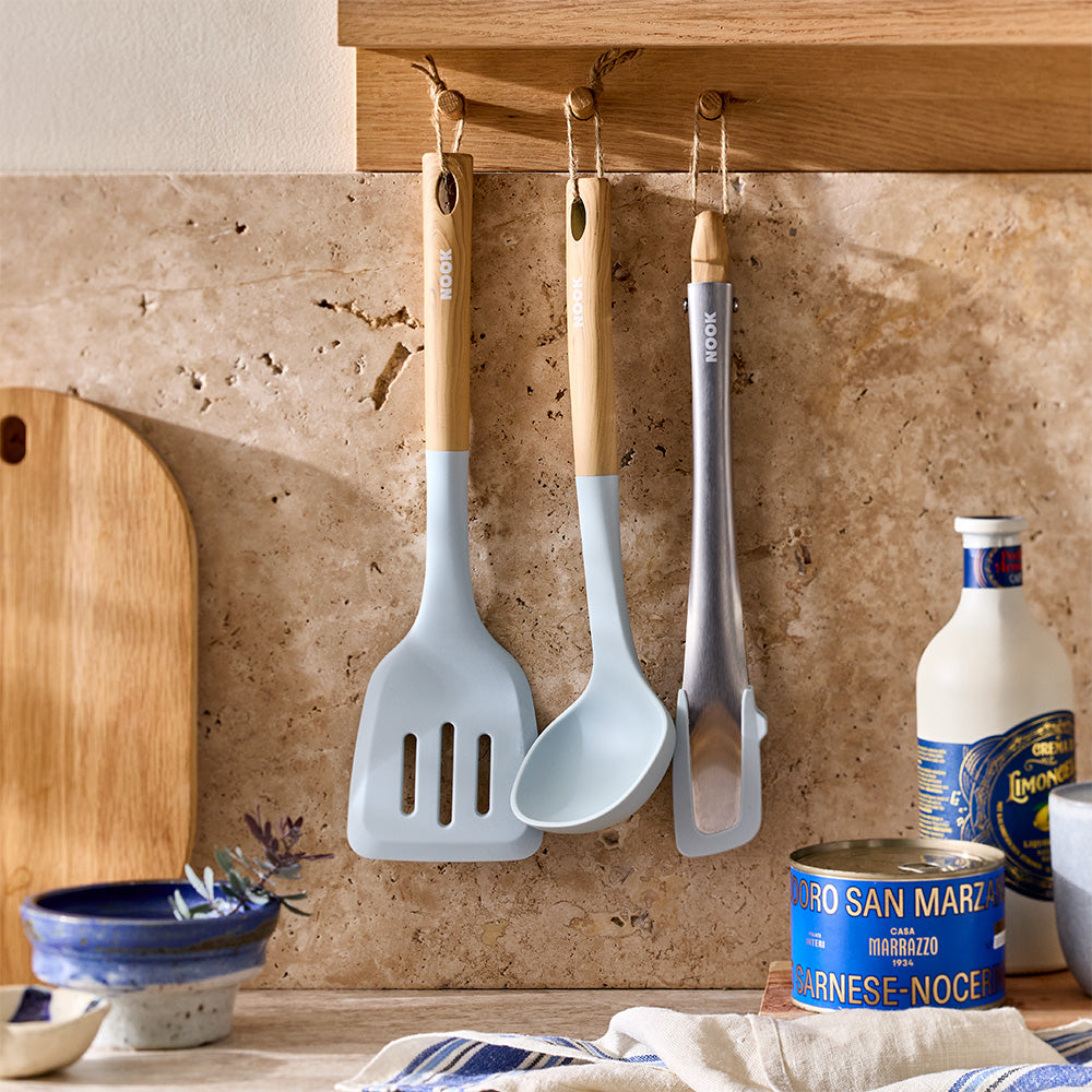 Light blue silicone kitchen utensils with wooden handles are hanging on hooks under a wooden kitchen shelf.