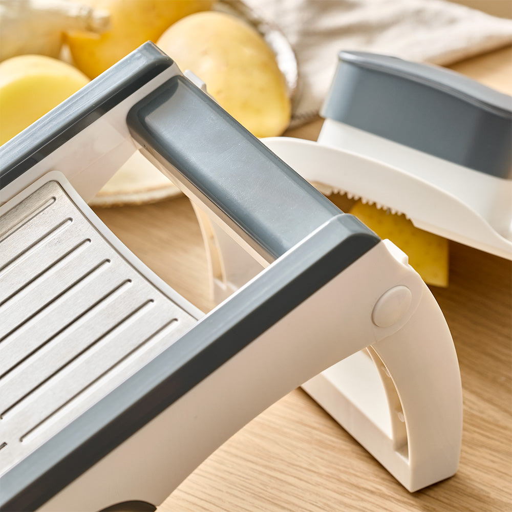 The top handle and upper frame of the mandoline slicer are shown resting near whole potatoes on a kitchen counter.