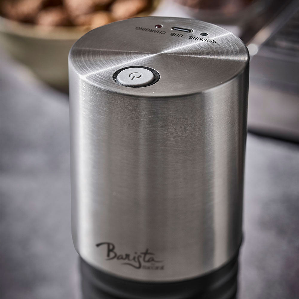 A close-up view of the top power button and stainless steel finish of the coffee grinder is shown against a dark, moody background.