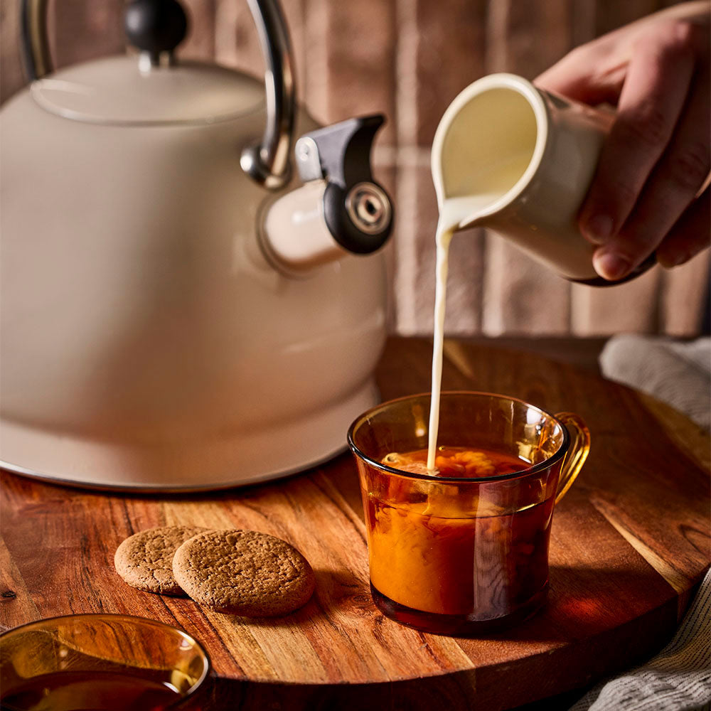 Milk poured into a freshly brewed cup of tea with the oat stovetop kettle to the side.