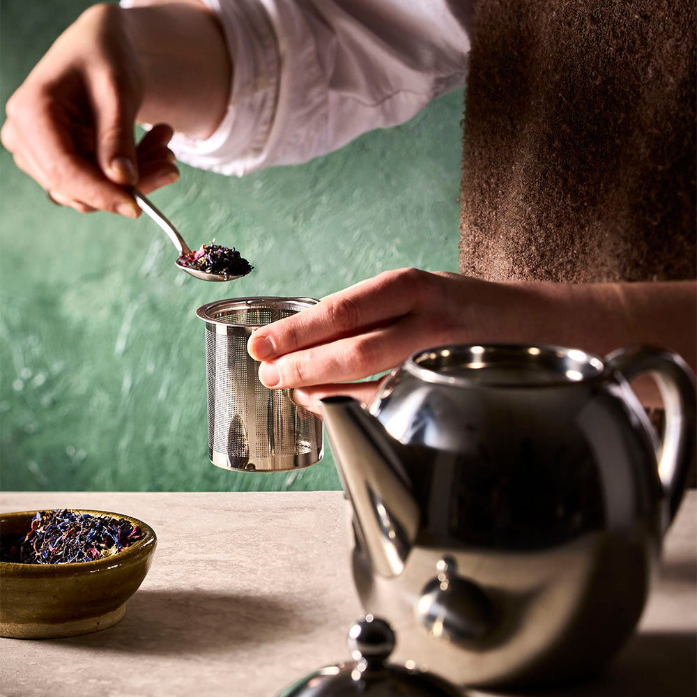Loose tea leaves being placed into the Barista stainless steel teapot infuser for brewing.