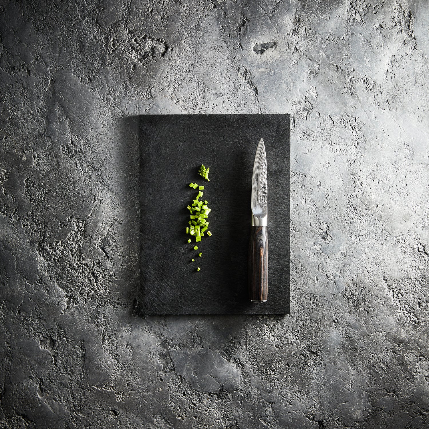 Chopped green herbs on a dark cutting board with a sleek silver knife - Baccarat Damashiro Emperor