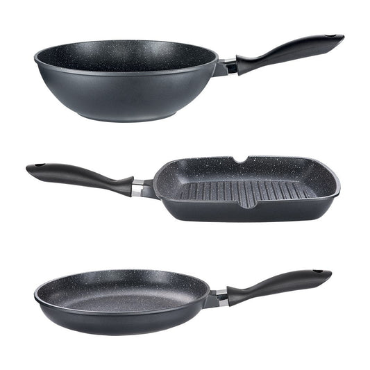 Three frying pans and a grill pan on a dark counter with wooden utensils and herbs - Baccarat