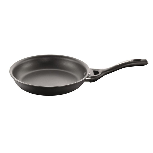 A black frying pan with vegetables including green peppers and tomatoes on a grey surface - Baccarat