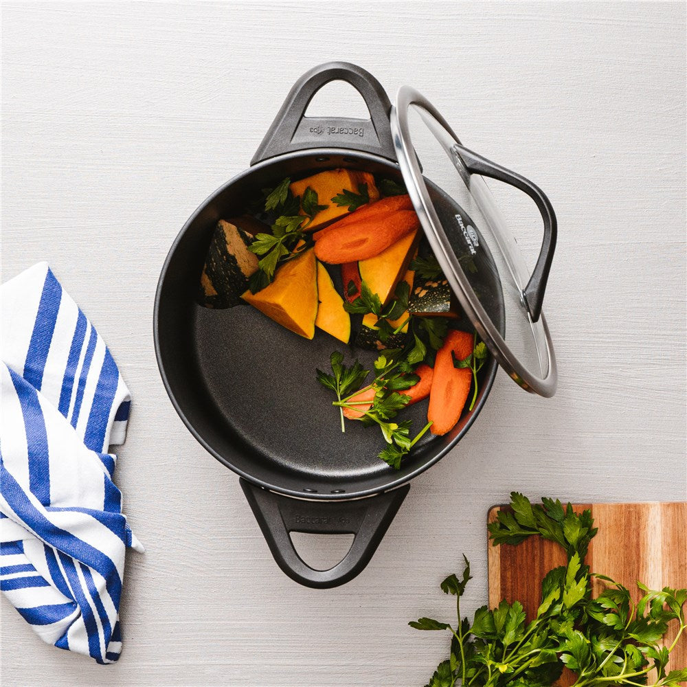 Round black stockpot with lid and bakelite handle filled with chopped carrots and greens - Baccarat