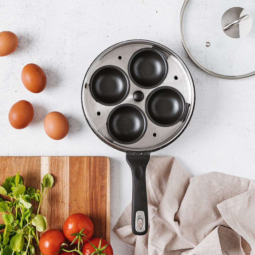 A sleek egg poacher with four sections surrounded by fresh eggs and greens - Baccarat granite