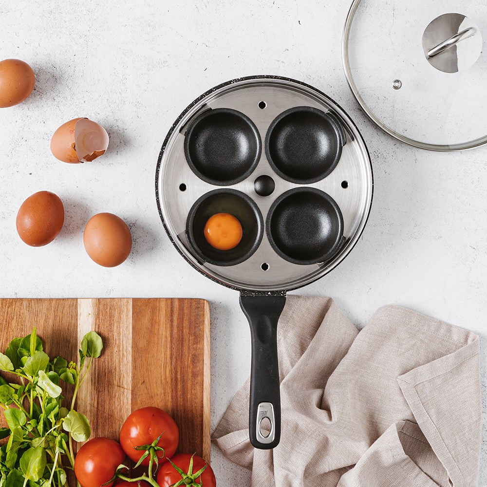 A sleek egg poacher with four sections surrounded by fresh eggs and greens - Baccarat granite