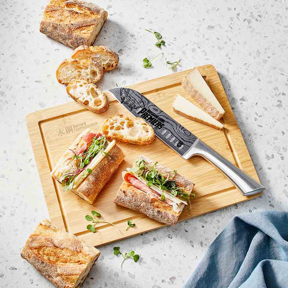 A freshly sliced sandwich on a bamboo cutting board with baguette slices - Baccarat Damashiro