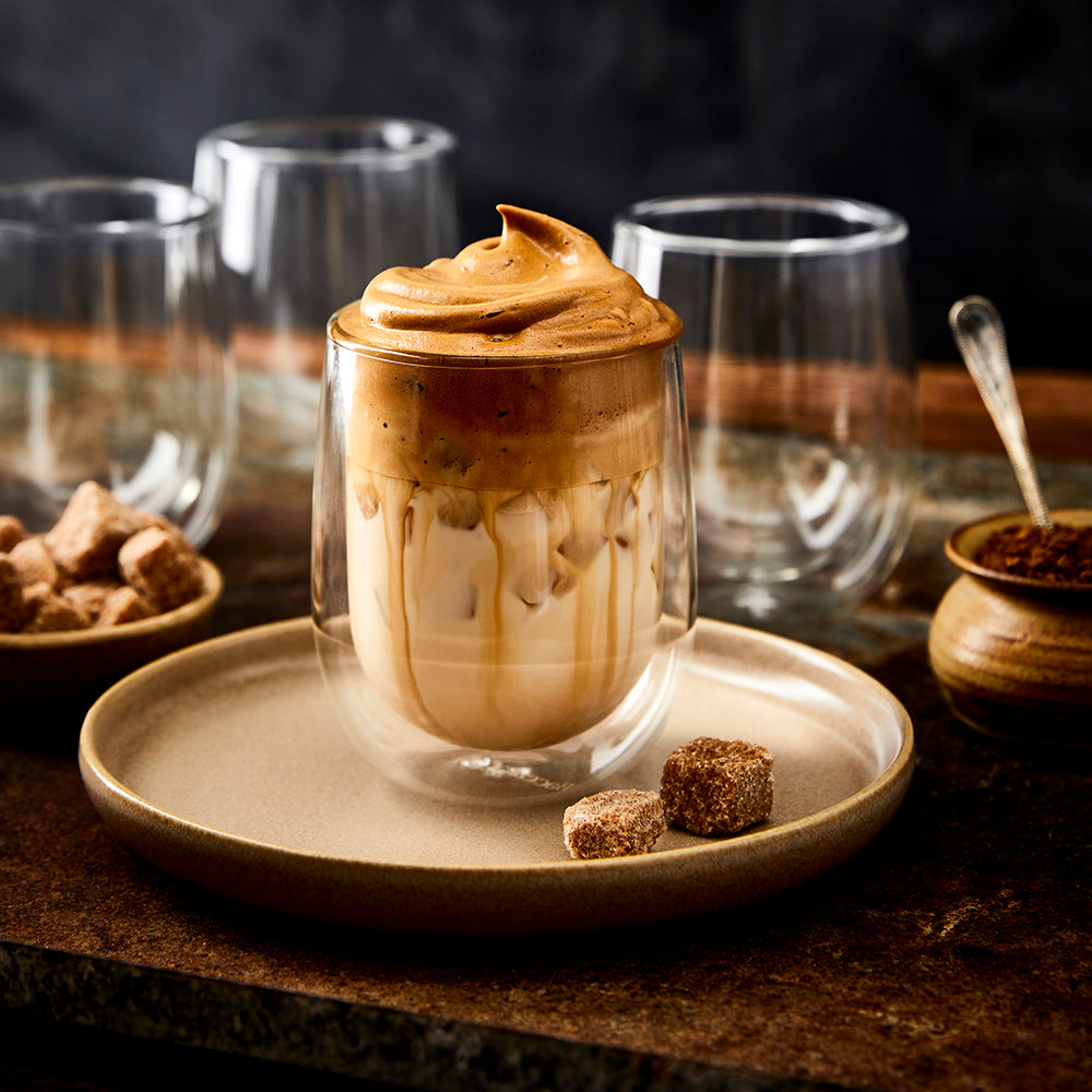 Dalgona coffee in double wall glass with empty glasses and sugar cubes - Baccarat Barista Cafe