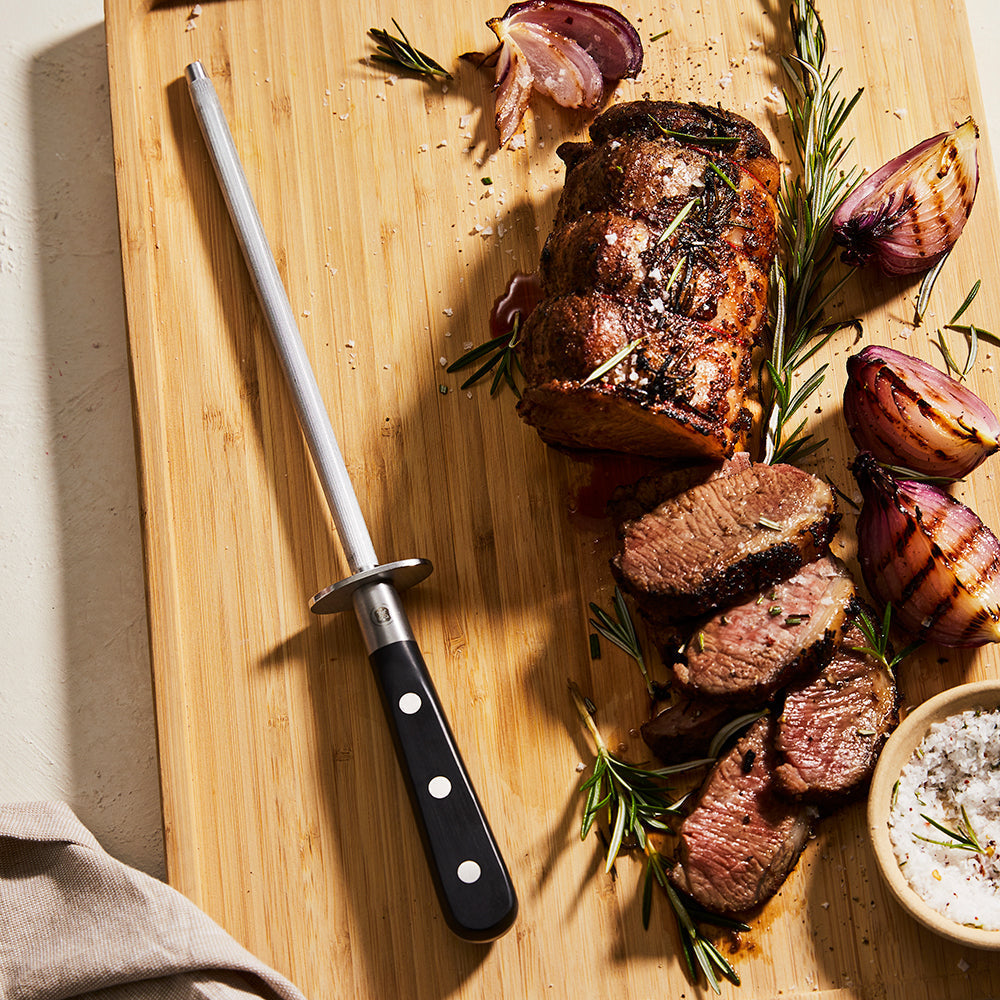 Sliced beef with rosemary and garlic on a cutting board alongside a Baccarat sharpening steel knife 
