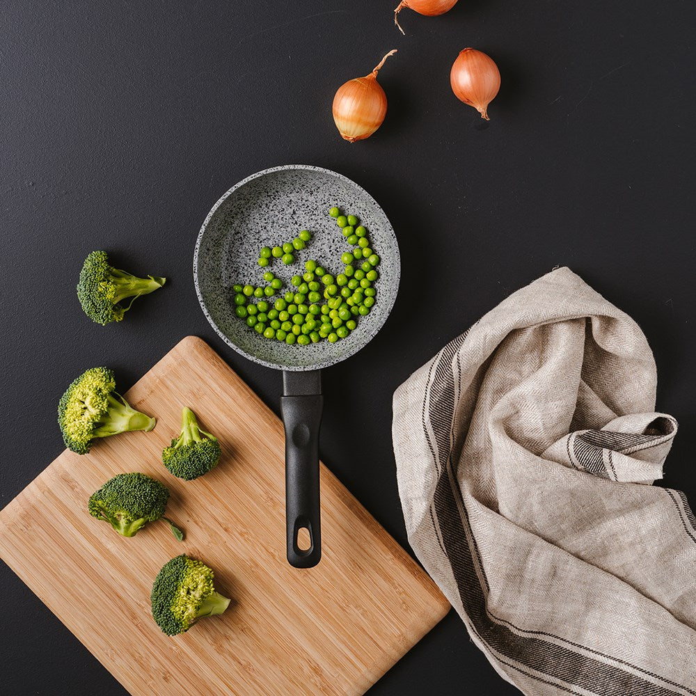 A black frying pan with green peas onions and broccoli on a wooden board 28cm frypan - Baccarat