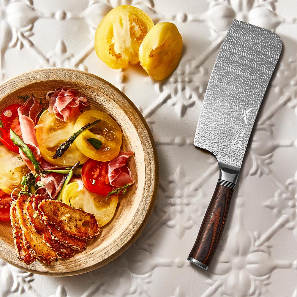 A hand slicing a red tomato with silver cleaver on a wooden cutting board  - Baccarat Le Connoisseur
