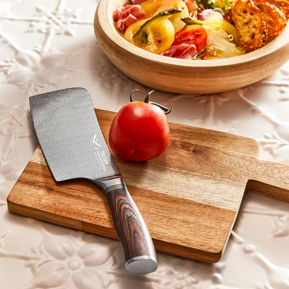 A hand slicing a red tomato with silver cleaver on a wooden cutting board  - Baccarat Le Connoisseur