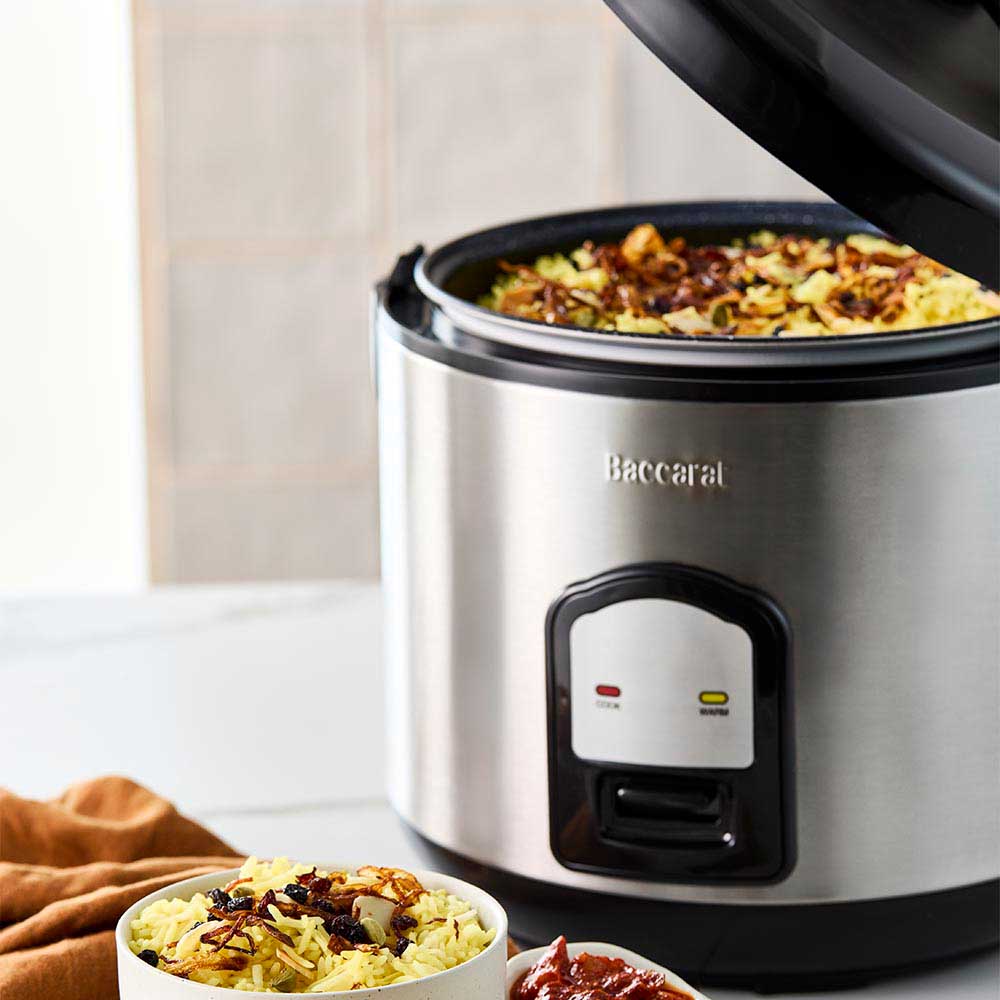 A person opening a silver rice cooker on a kitchen counter next to a bowl of veggies- Baccarat