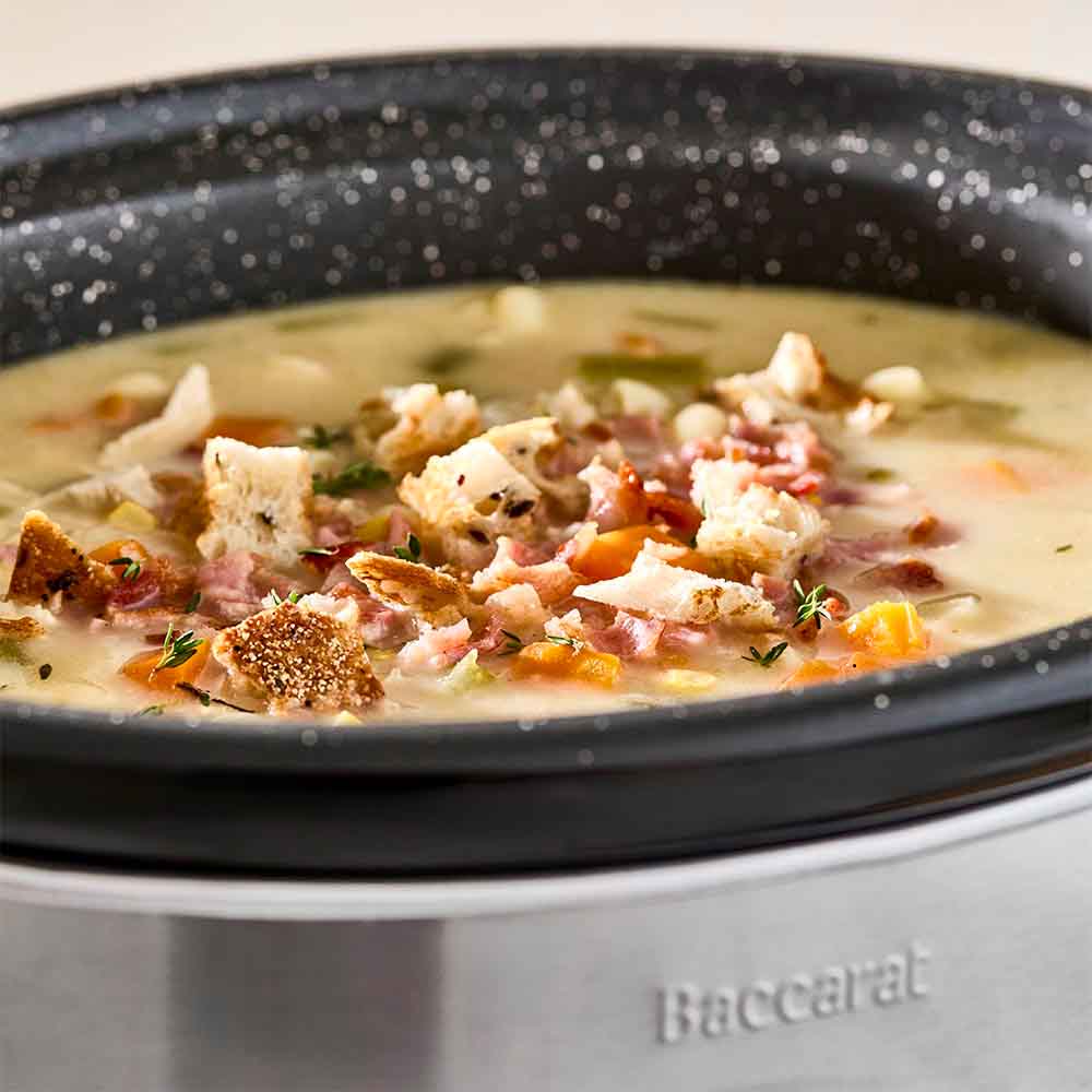 A vibrant orange creamy soup garnished with fresh parsley in a sleek bowl - Baccarat the Tasty Chef