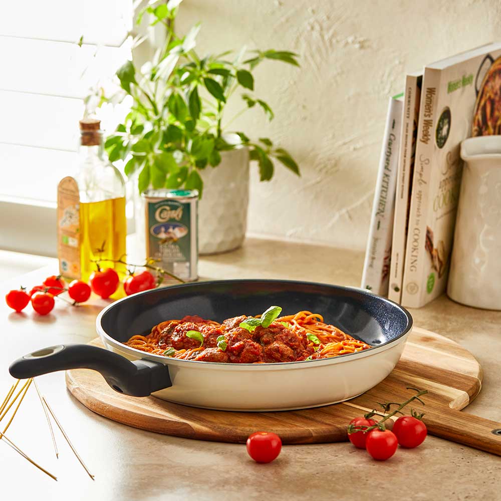 A 32-cm Baccarat  Bio Frying pan containing pasta on a wooden board surrounded by fresh ingredients
